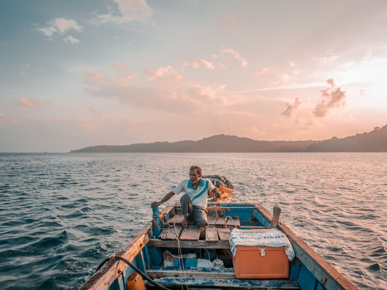 Home A lone fisherman navigates the calm waters of the Andaman Sea at sunrise, setting out for a day of adventure.