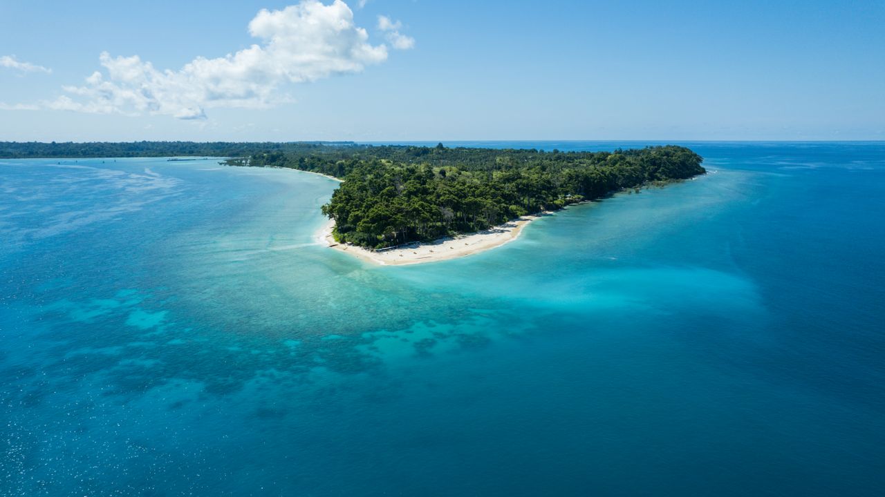 Home Stunning drone view of Kadamtala Island with clear blue waters and lush greenery in India.