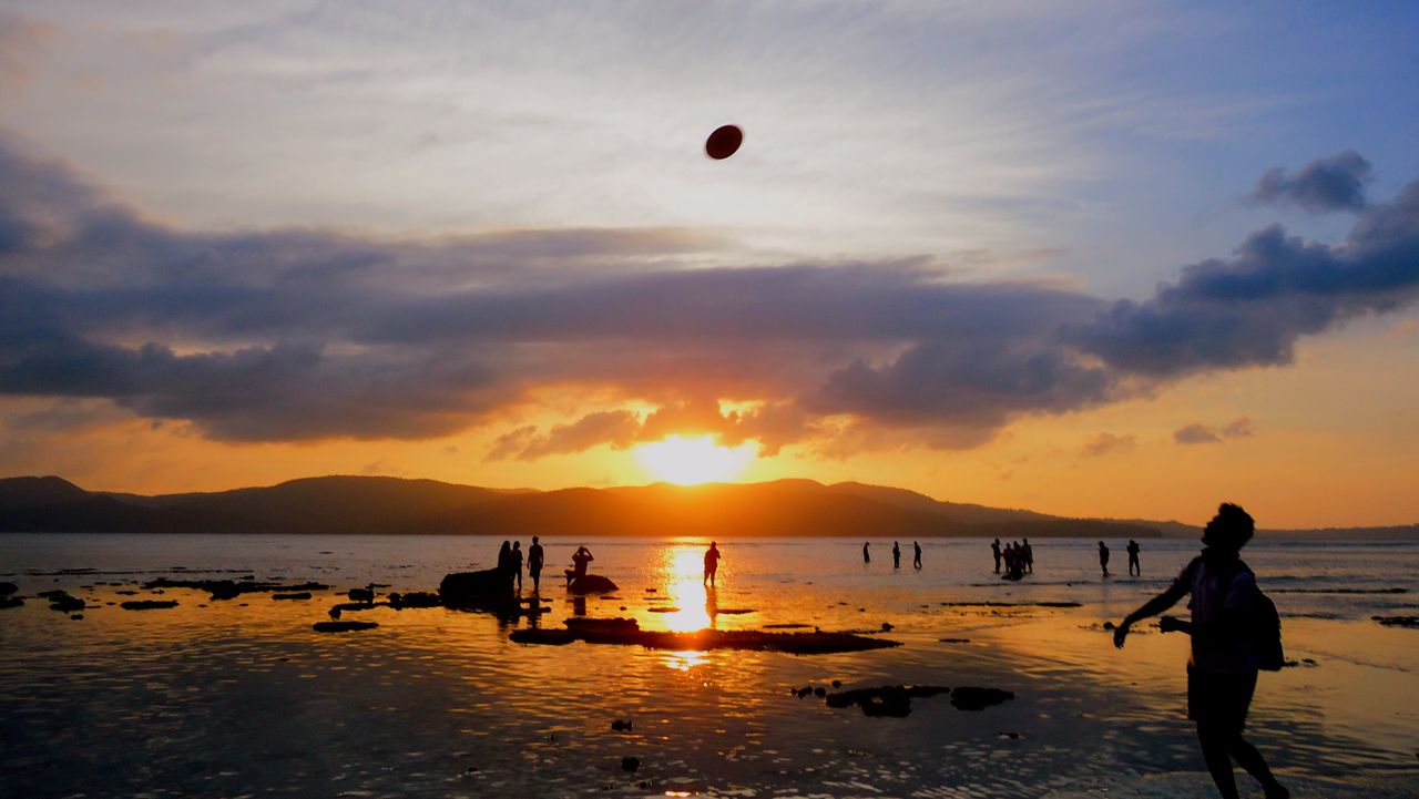 Home Silhouettes of people enjoying a sunset at a picturesque beach in Port Blair, India.